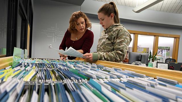 Student and career development staff member looking into a file cabinet.